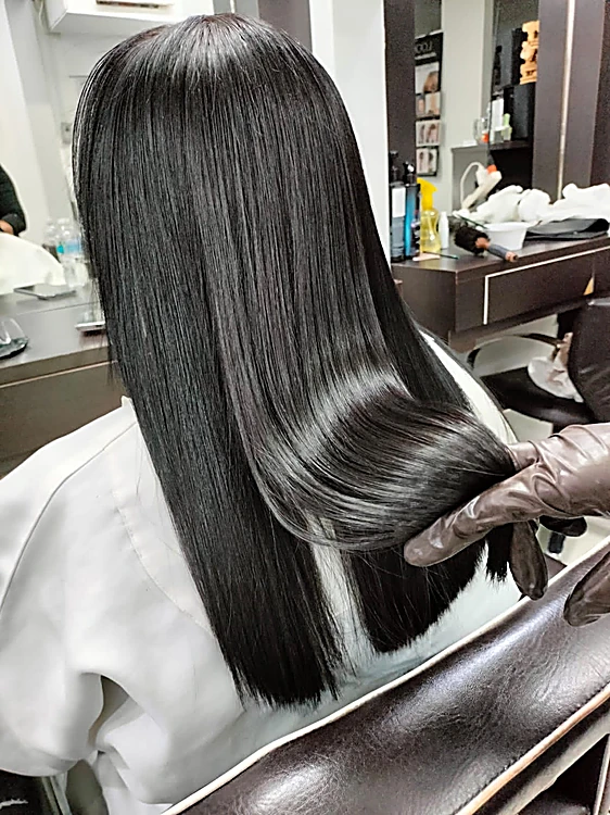 Cabello negro largo, alaciado y con brillo, visto de espaldas en la silla del salón mientras la estilista lo acomoda