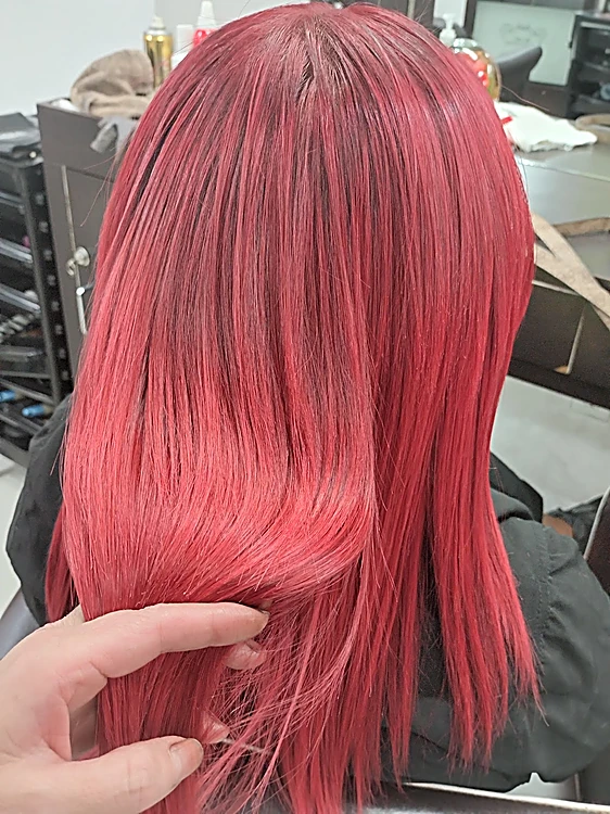 Cabello lacio rojo coral a media espalda, la estilista sostiene un mechón