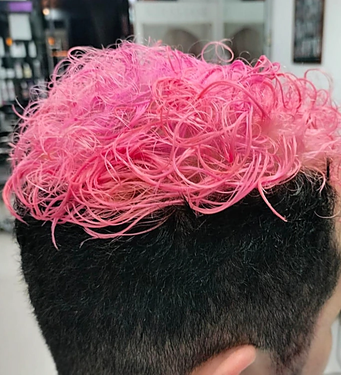 Corte de caballero con laterales cortos y rizos teñidos de rosa en la parte de arriba, visto por detrás