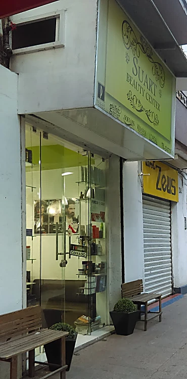 Fachada del salón en Londres 204: caja verde limón con el letrero Suart Beauty Center sobre una puerta de vidrio y una banca de madera en la banqueta